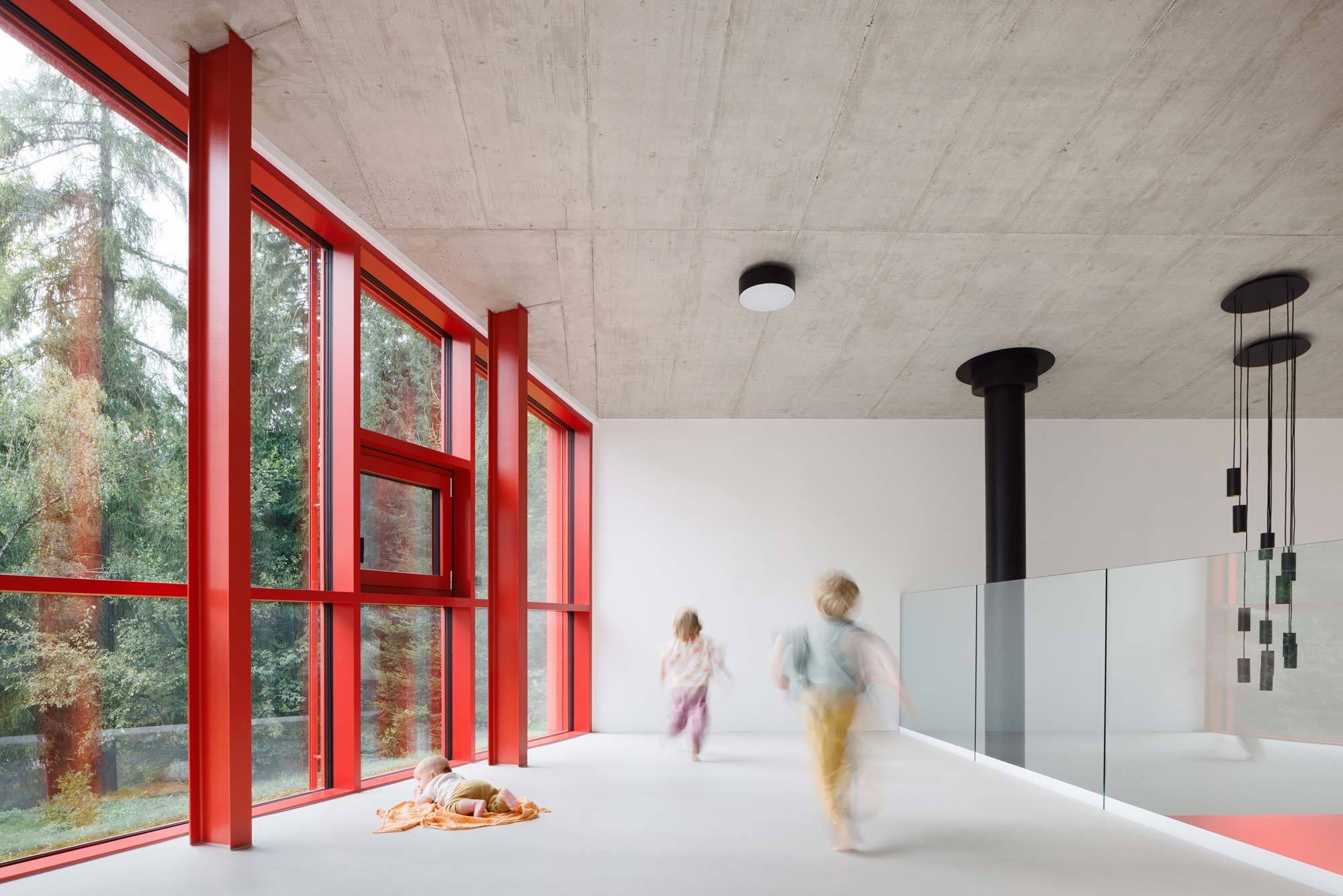 Alle anderen sehen rot: Während der Bau durch seine auffällige Farbe von außen dominant und laut wirkt, bestimmen helle, ruhige Oberflächen und gerahmte Ausblicke in das dichte Grün den Innenraum.