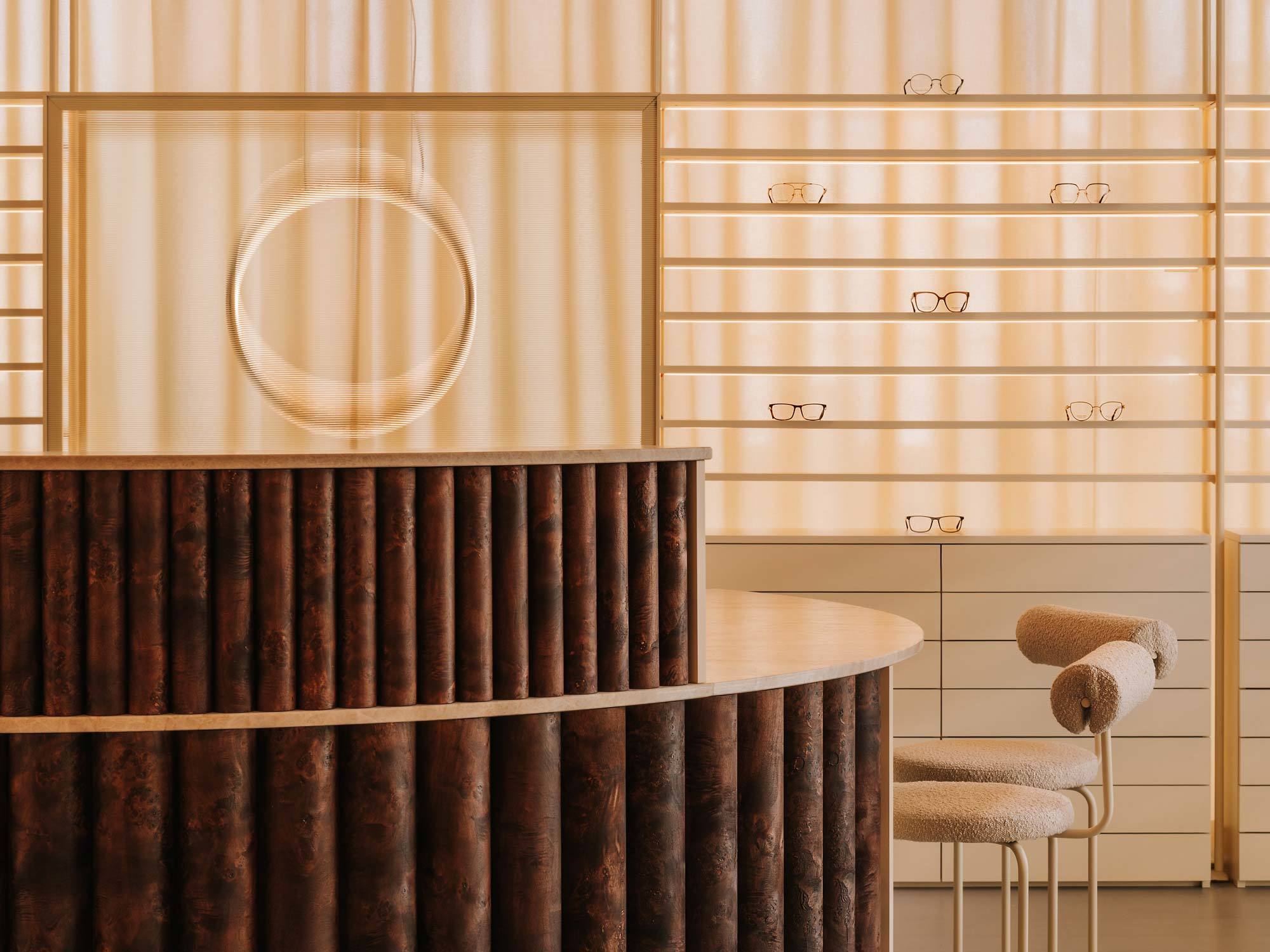 Der runde Tresen bildet den zentralen Anlaufpunkt von AUGA, einem Optikerladen im polnischen Breslau. Die schwebende Lichtskulptur ist der Makula des menschlichen Auges nachempfunden.