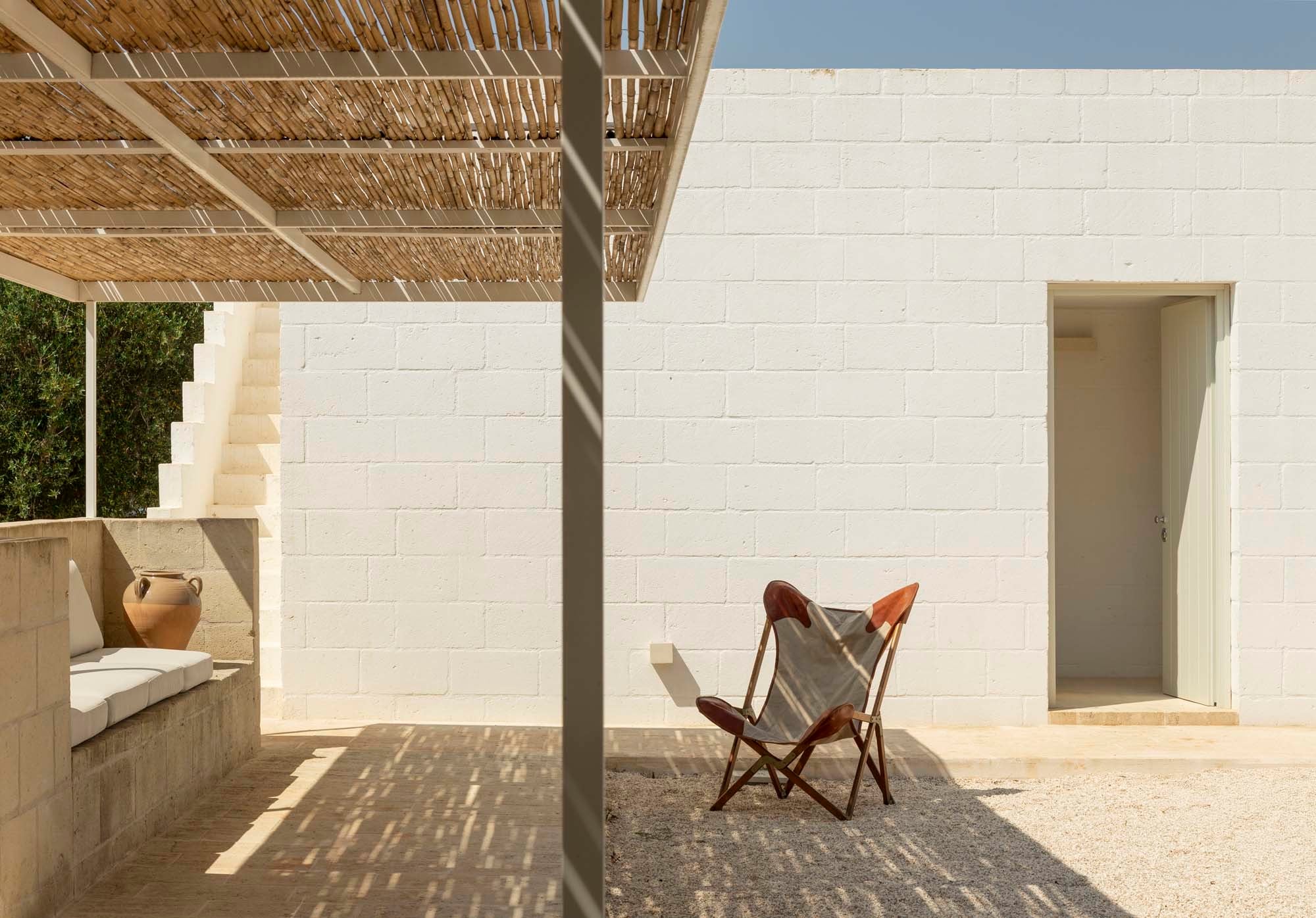 Unter einer Pergola finden Urlauber*innen Schatten. Die gemauerte Bank nimmt die Ästhetik des Neubaus auf.