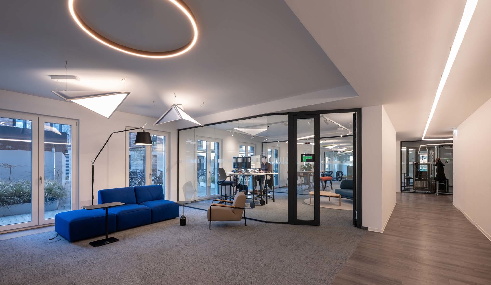 Der offene Bereich wird von vier Leuchtenserien von Artemide geprägt: A.24 Stand-alone Ceiling Circular leuchtet die Lounge aus, die Pendelleuchten Flexia absorbieren zusätzlich Gesprächsschall und Tolomeo Mega Terra spendet direktes Licht beim Sofa. Rechts begleitet Alphabet of Light den Weg durch den Flur.