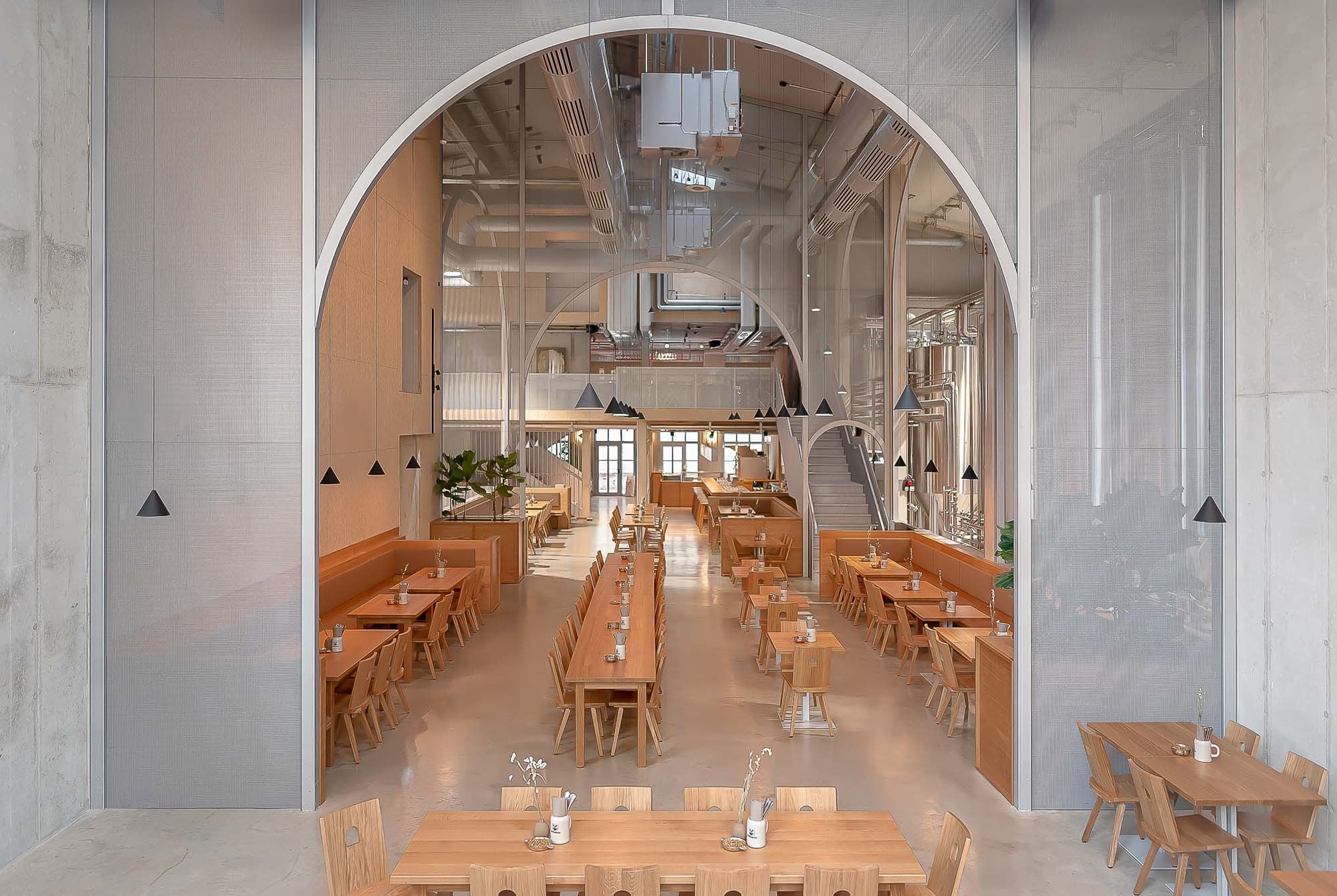 Der zentrale Gastraum des Müllerbräu Sudhauses ist als dreischiffige Halle organisiert – Gastronomie im Mittelschiff, Braubehälter sichtbar in den Seitenschiffen.