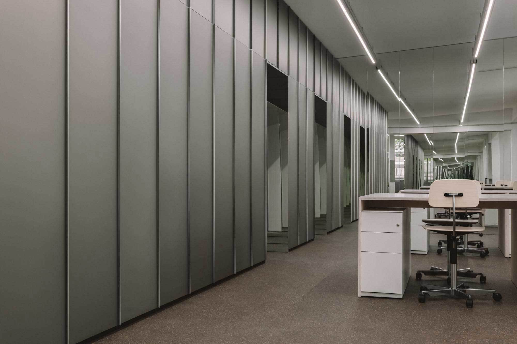 Bürobereich im Erdgeschoss: Metallverkleidete Wände im 60-Zentimeter-Raster, durchlaufende LED-Lichtlinien und eine Spiegelwand im Hintergrund, die den Raum in die Tiefe erweitert