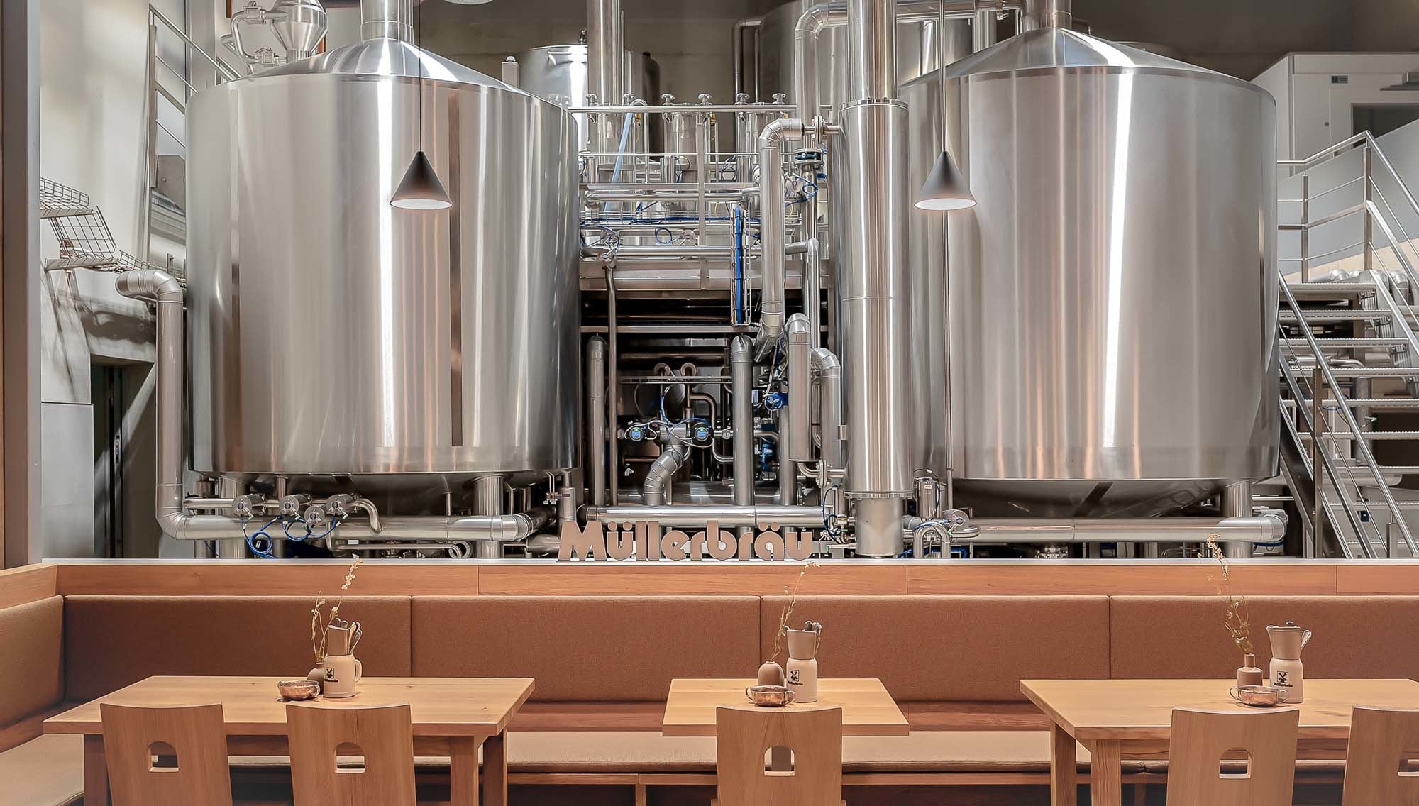 Unmittelbare Nähe zum Brauprozess: Sitzbänke und Tische aus Eichenholz stehen den Edelstahl-Gärtanks direkt gegenüber und machen die Produktion zum integralen Bestandteil des Gastroraums.