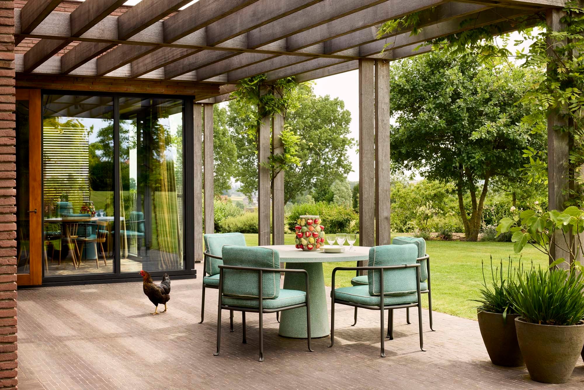 Eine mit einer Pergola überdachte Terrasse wird dank der großen Fenster optisch Teil des Raums.