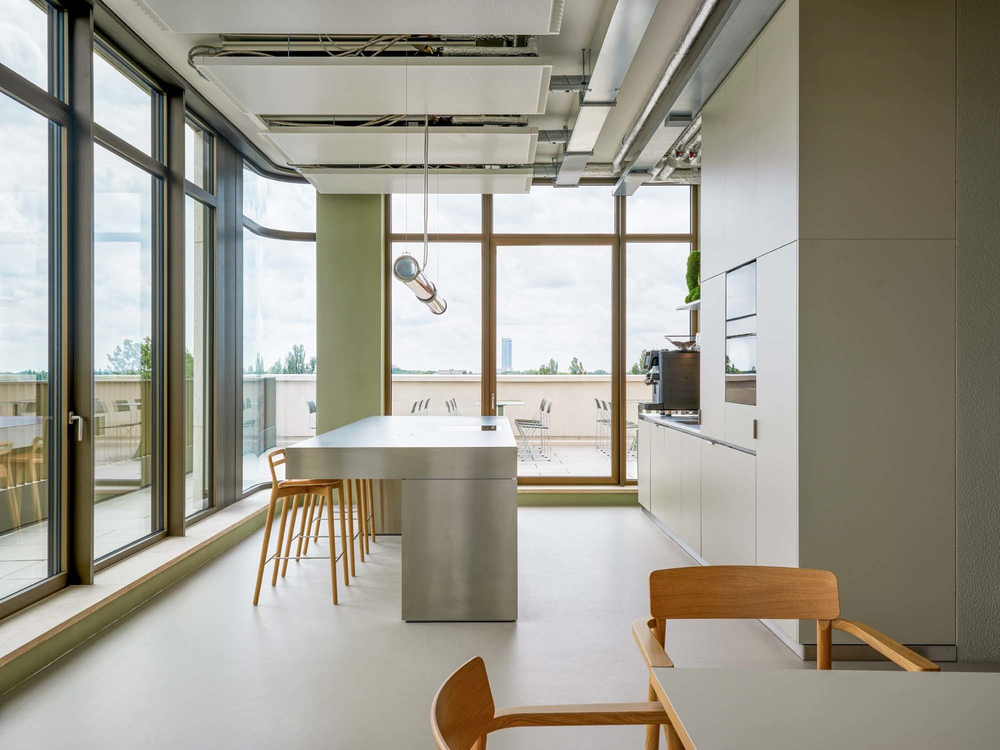Die Cafeteria spiegelt das kommunikative Bürokonzept wider und liegt in einer Gebäudeecke mit Ausblick und Zugang zur Dachterrasse.