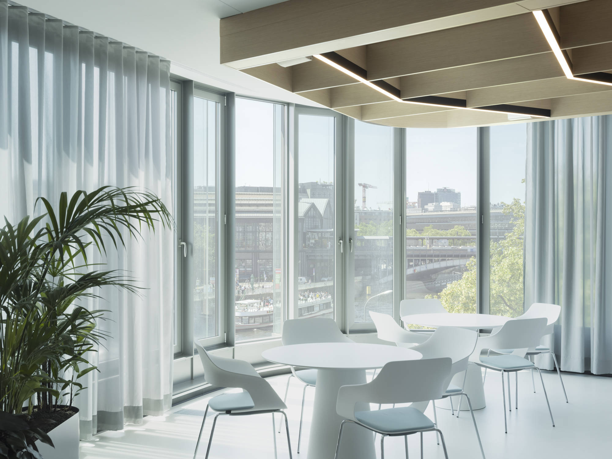 Das Bistro im Raum mit der gebogenen Glasfassade bildet das Herzstück der neuen Arbeitswelt; der Blick auf die Spree schafft eine einladende Atmosphäre für Austausch, Pausen und informelle Treffen.