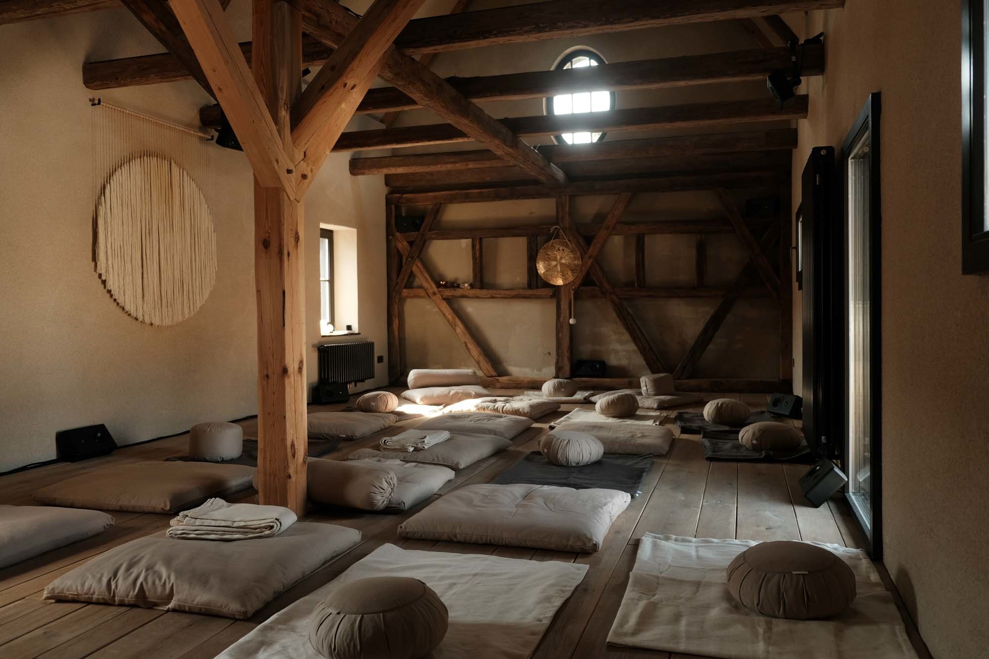 Meditations- und Rückzugsraum im ehemaligen Pferdestall: Freigelegtes Fachwerk, weiche Bodenkissen und natürliche Materialien schaffen eine ruhige Atmosphäre.