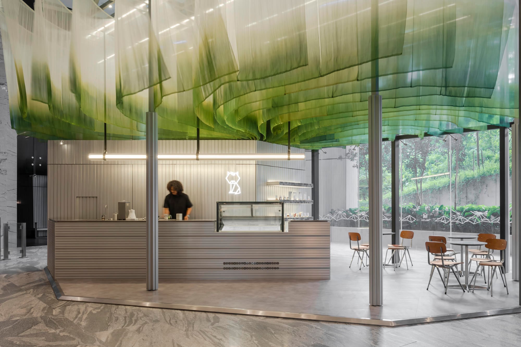 Eine schwebende Seidenwolke, diffuses Licht und Aluminiummöbel verwandeln das Matcha-Café Niko Neko in Malaysia in ein poetisches Labor für Teetradition und Färbehandwerk.