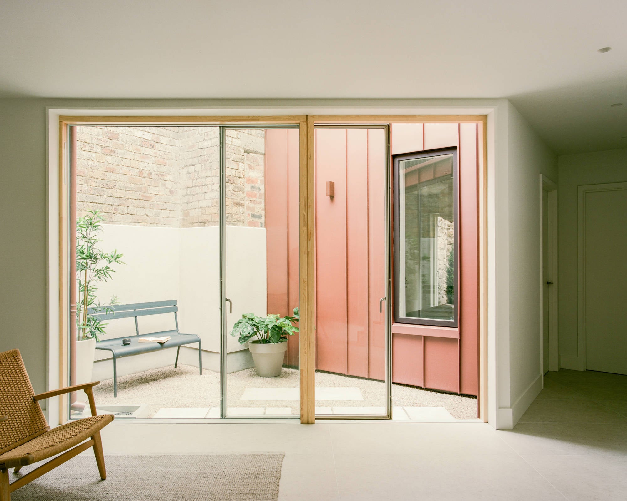 Durch raumhohe Holzrahmen-Schiebetüren öffnet sich der Wohnbereich auf den intimem Innenhof mit lachsfarbener Verkleidung.